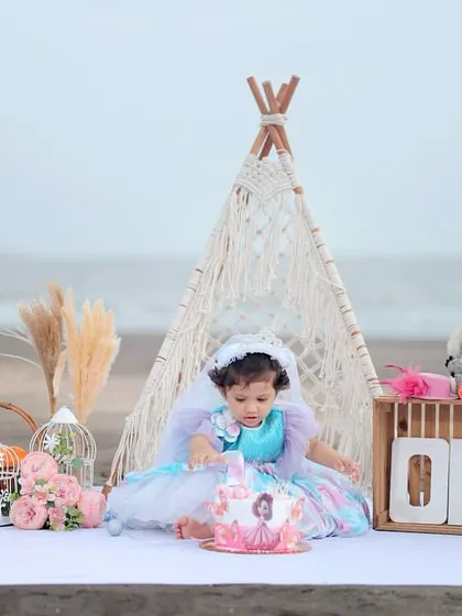 A beautiful boho-themed cake smash on the beach, with a teepee, pampas grass, and floral decorations.