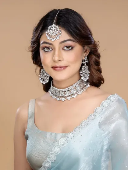 A model looks directly at the camera, showcasing a stunning silver-toned choker, maang tikka, and earrings set. The clean background and confident pose make this a perfect image for a modern ethnic jewellery catalogue.