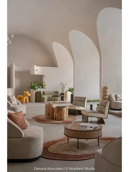 A full view of the "Vault's Up" experience center. The interior is a blend of modern minimalism and organic warmth, with curved archways, a neutral lime plaster finish, and natural elements like handcrafted wooden stools and lush greenery.
