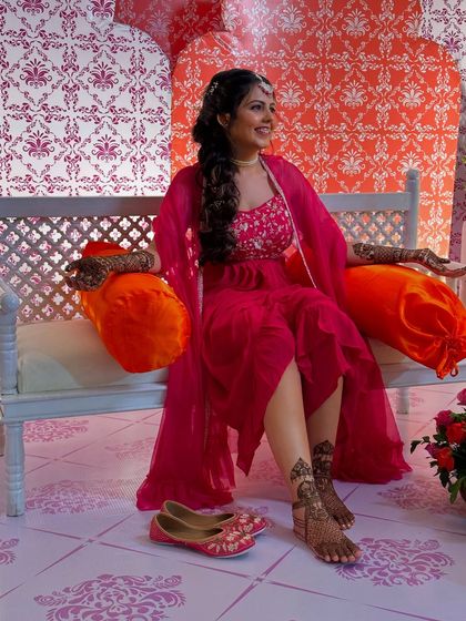 A happy bride showing off her full set of mehndi, including detailed work on her feet. The design complements her festive attire perfectly.