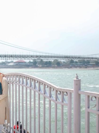 An intimate embrace by the railings overlooking the Ganga, with the Ram Jhula bridge in the distance. This captures a quiet, romantic moment in an iconic Rishikesh location.