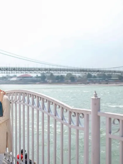 An intimate embrace by the railings overlooking the Ganga, with the Ram Jhula bridge in the distance. This captures a quiet, romantic moment in an iconic Rishikesh location.
