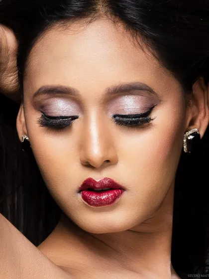 A close-up beauty shot in color, focusing on the model's metallic eyeshadow and bold red lips. The lighting perfectly captures the makeup's texture and pigment.