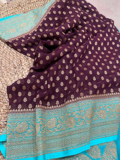 A lovely wine-purple pure Banarasi Kadi georgette saree with a contrasting sky blue border. The gold butis and woven border make it a very elegant choice.