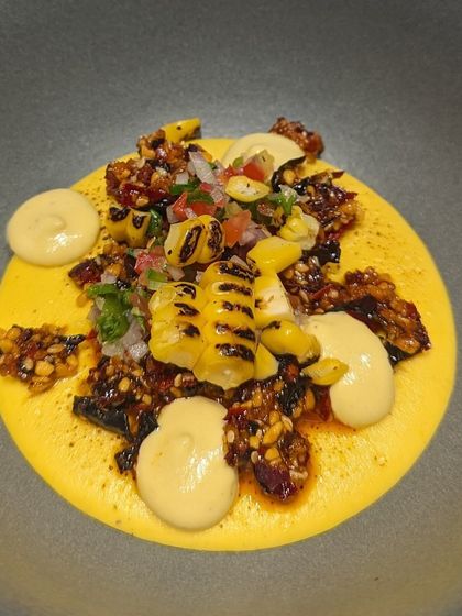 A vibrant dish of charred corn with a creamy corn puree and a savory cacao brittle. This plate was part of a menu exploring the connection between corn and cacao, two staples of ancient Mesoamerican cuisine.
