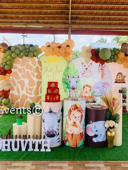 An outdoor jungle theme setup on an artificial grass mat. The decor uses earthy tones, animal print backdrops, and cute cartoon animal props, perfect for a daytime celebration.
