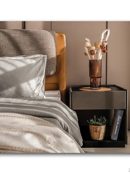A beautifully styled bedside table, where textures and natural elements take center stage. The morning light highlights the fabric of the headboard, the dried flowers in the vase, and the small plant, creating a cozy and serene vignette.