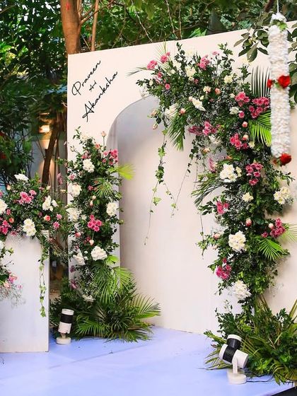 A beautiful floral archway serves as a photo backdrop. The combination of pink and white flowers with lush greenery is both romantic and elegant.
