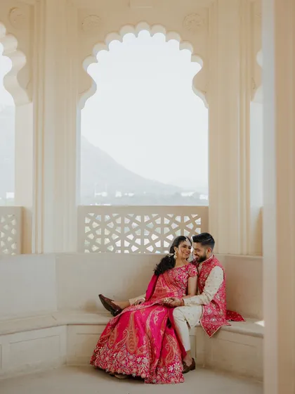 A sweet, happy moment between a couple during their Haldi ceremony in Udaipur. Seated in a palace alcove, their vibrant pink outfits pop against the neutral stone, capturing the joy of the celebration.