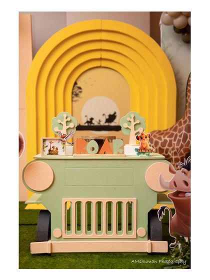 The centerpiece of our Lion King party is this custom-built safari jeep dessert table. The backdrop features a stunning silhouette of Simba, Timon, and Pumbaa against a yellow sunset.