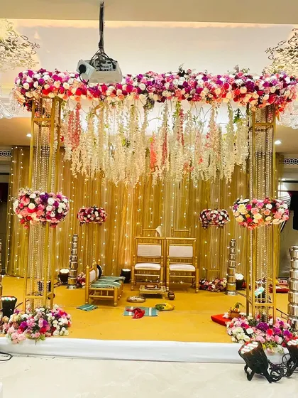 A classic mandap design featuring a gold metal frame, a canopy of hanging florals, and a shimmering backdrop. This setup is perfect for couples who want a blend of traditional and glamorous elements.