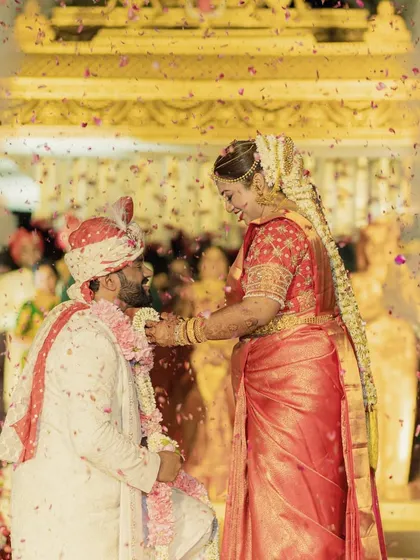A beautiful moment from a South Indian wedding ceremony. The couple exchanges garlands under a shower of petals, surrounded by the warmth of their loved ones.