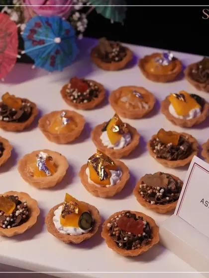 A platter of assorted miniature tarts, beautifully decorated with fresh fruit and edible gold leaf. Each one is a bite-sized piece of heaven.