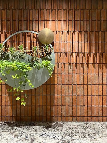 A wider view of the atrium wall art. The planter, with its trailing greenery, brings a refreshing oasis of life to the warm, earthy tones of the exposed brick.