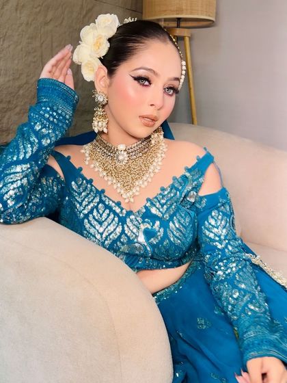 A close-up of the teal blue lehenga, showing the pearl jewelry and floral hair accessory.