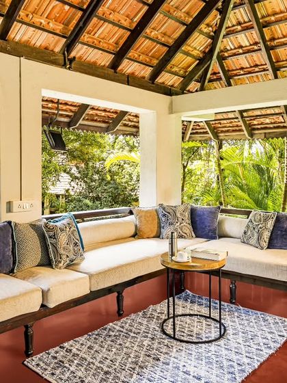A cozy corner of a veranda lounge, decorated with plush cushions. The open windows offer an uninterrupted view of the lush greenery outside, bringing the outdoors in.