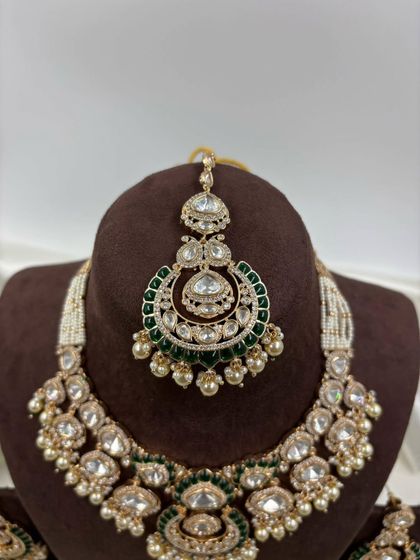 One of our most requested bridal sets, this design features large uncut Kundan stones, green Meenakari work, and pearl detailing. The set includes a necklace, chandbali earrings, and a matching maang tikka.