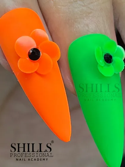 A close-up of our neon orange and green nails with 3D floral accents, showcasing the sharp stiletto shape and matte finish.