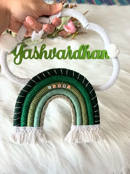 A close-up of the 'Yashwardhan' name hanging, showing the detail of the name beads woven into the green rainbow.