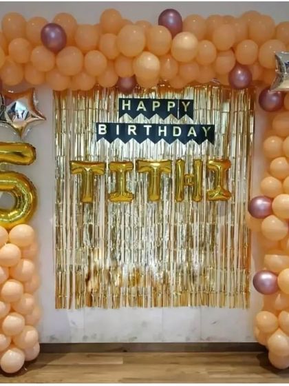 A simple backdrop decoration with a gold fringe curtain and a peach and purple balloon frame for a 5th birthday.