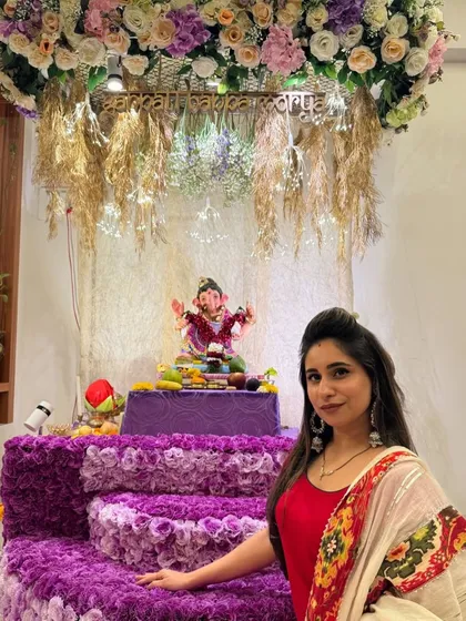 This Ganpati setup combines a rich purple floral base with a canopy of pastel flowers and rustic dried grasses. The "Ganpati Bappa Morya" sign adds a beautiful, personalized touch to the decor.