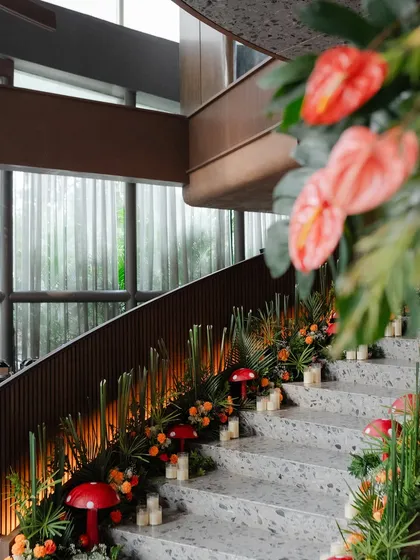 The staircase decorated with a lush runner of tropical greens, orange florals, and red mushroom props, lit by the warm glow of candles.