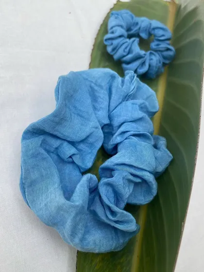 A set of two scrunchies, one large and one small, made from fabric dyed with natural indigo. They are a simple and stylish way to add a touch of handmade beauty to your hairstyle.