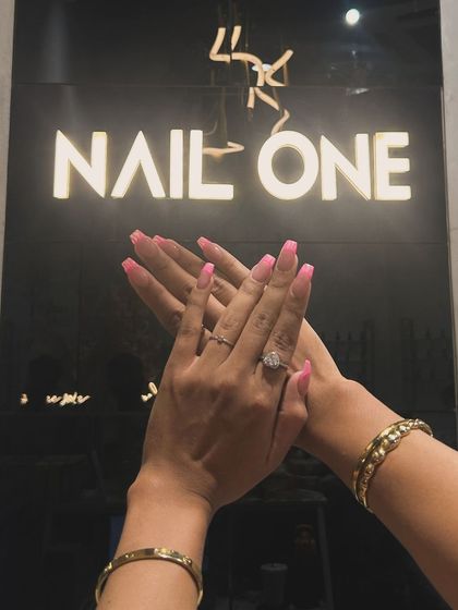 A client showing off her fresh pink manicure against our salon's branded wall. We love seeing you celebrate your new nails.