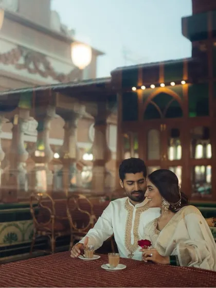 A romantic coffee date moment. This photo, taken through a window, adds a dreamy, cinematic quality to the pre-wedding shoot, telling a story of shared quiet moments.