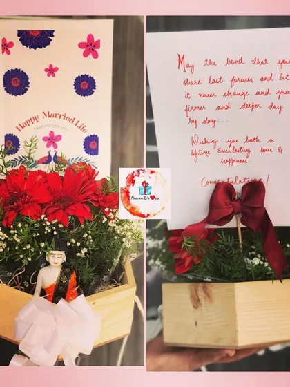 A beautiful wedding gift celebrating a "Happy Married Life." This hamper features a wooden planter with bright red flowers, a decorative figurine, and a heartfelt, handwritten congratulatory note.