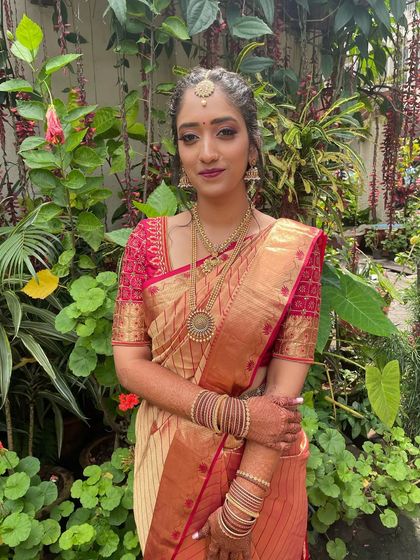 A full-length view of Dr. Rakshitha's first look. The traditional red and gold saree is perfectly balanced with the modern, smokey eye makeup.