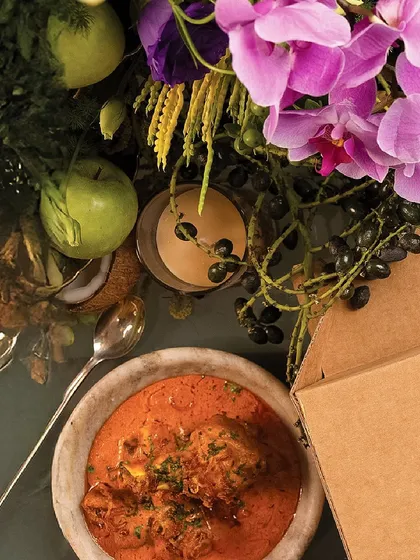 An overhead shot showing our food alongside our signature Dinner Box, surrounded by lush flowers, capturing the essence of a luxury delivery experience.