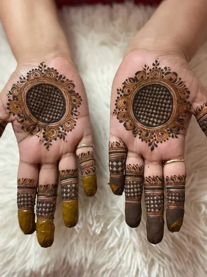 A classic mandala design with a checkerboard pattern filling the center. The dark, solid fingertips are a traditional touch that makes the detailed work on the palm stand out.
