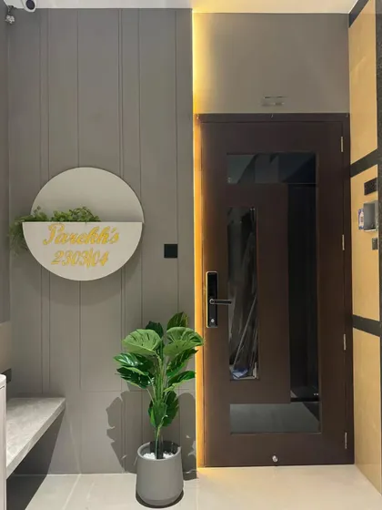 A modern and minimalist entrance that perfectly blends sophistication with warmth. Featuring a sleek veneer door, soft grey panel walls, and subtle natural touches like a custom nameplate with a built-in planter.