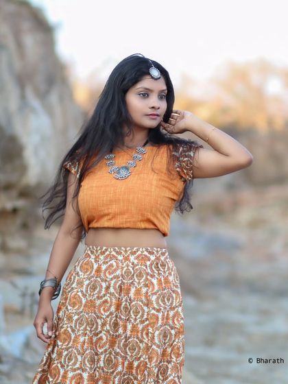 A thoughtful pose in a rustic outdoor setting, with the traditional outfit complementing the natural tones of the environment.