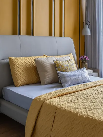 A close-up of the vibrant yellow bedroom, showing the texture of the woven bedding and the basketweave pattern on the accent pillows. The fluted wall paneling adds another layer of detail.