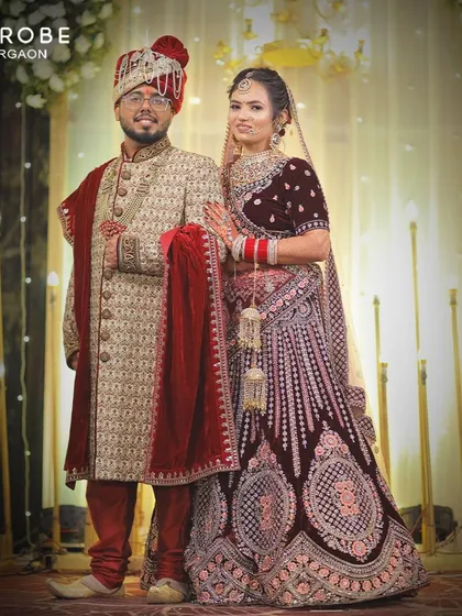 A coordinated couple look that spells royalty. The bride is in a deep maroon velvet lehenga, and the groom wears a matching sherwani, ready for their grand entrance.