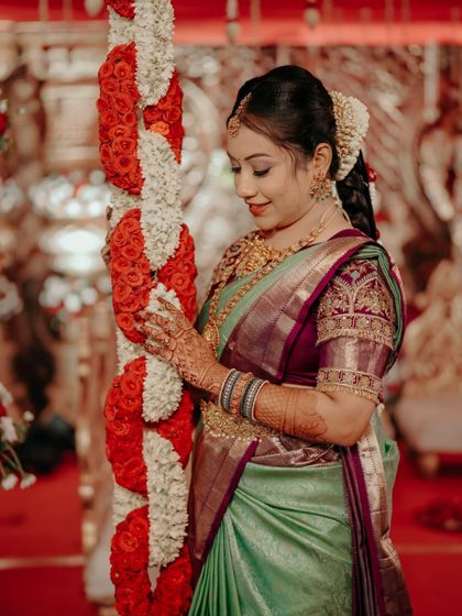 A bride posing with a pillar of flowers, her green and purple saree looking stunning against the decor.