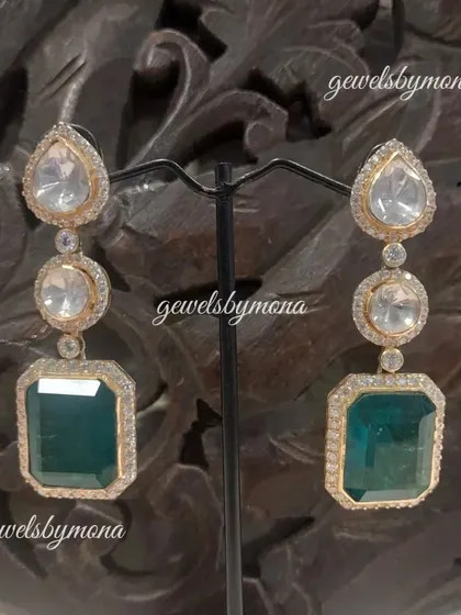 These long drop earrings feature a line of polki stones culminating in a large, rectangular emerald. They are the epitome of elegance and are perfect for a sophisticated evening look.