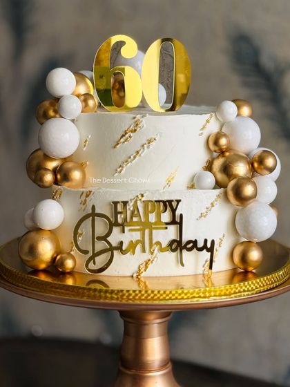 A glamorous two-tier cake for a 60th birthday celebration. The white and gold design is both modern and elegant, decorated with shimmering gold and white spheres for a festive touch.