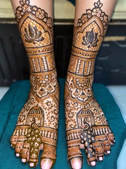 A close-up of bridal feet mehandi featuring beautiful peacock and lotus motifs. The fine line work and shading create a rich and detailed design.