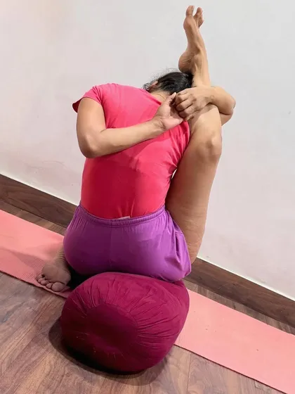 This is an advanced hip-opening and forward-bending pose. The use of a bolster provides support, allowing the practitioner to surrender more deeply into the asana and release tension in the hips and spine.