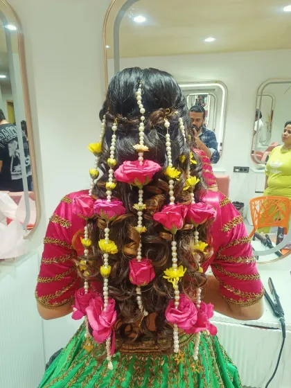 For a vibrant Mehendi function, I created this playful and intricate hairstyle featuring cascading curls and braids. The style is heavily adorned with strings of pearls and bright pink and yellow fresh flowers.