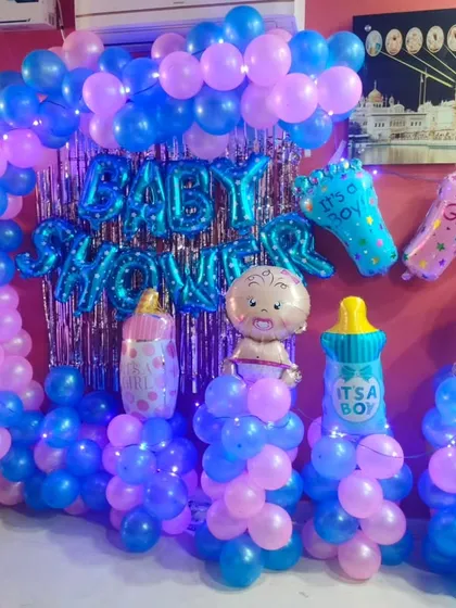 A vibrant baby shower decoration at home. This setup features a blue and pink balloon arch against a shimmer curtain, with lots of fun baby-themed foil balloons.