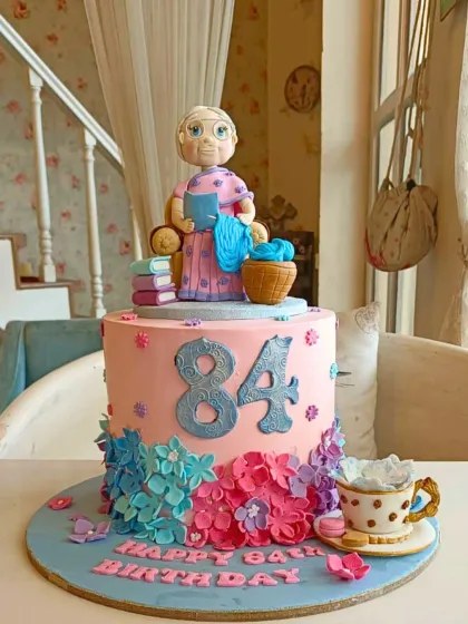 A heartfelt 84th birthday cake for a grandmother who loves to knit, featuring a fondant figure, books, and a cascade of flowers.