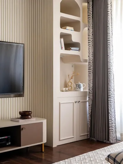 Another view of the bedroom, showing the custom shelving unit next to the television. The vertical fluting on the wall adds texture and visual interest.