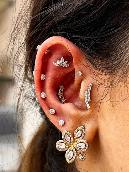 This client wanted a full, sparkling look. We created a constellation of diamond-simulant studs running up the ear, anchored by a large, glamorous floral earring on the lobe.