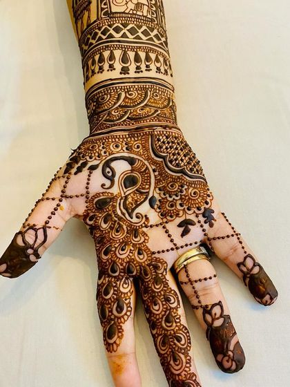 A detailed peacock design on the back of the hand, complete with a delicate beaded chain (jaali) pattern extending to the fingers.