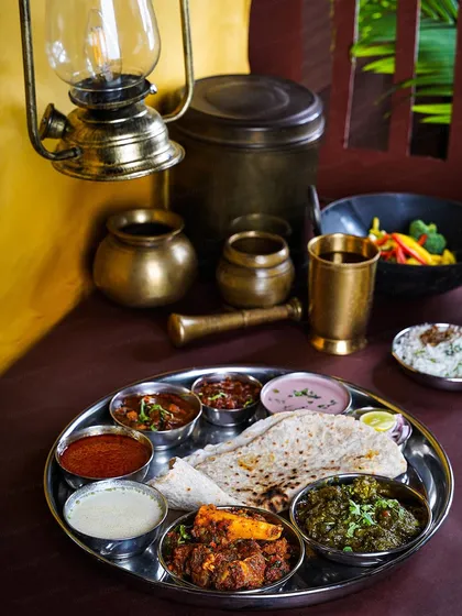 A full Maharashtrian non-vegetarian thali served in a rustic setting with an oil lamp. This shot captures the complete dining experience, full of warmth, tradition, and flavor.