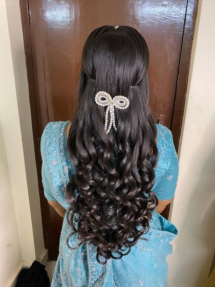 A stunning reception hairstyle featuring perfectly defined curls and a half-updo, finished with a modern pearl bow clip.